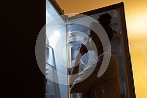 Young girl looking in fridge at night.