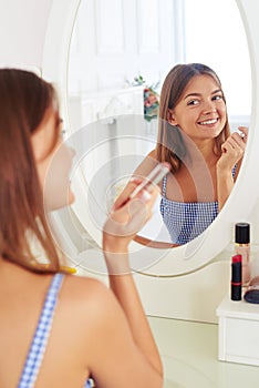Young girl is looking at the mirror and holding a lipstick