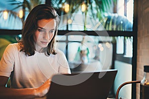 Young girl looking on screen monitor using laptop at cafe workplace, hipster freelancer typing on keyboard  laptop indoors