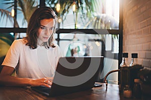 Young girl looking on screen monitor using laptop at cafe workplace, hipster freelancer typing on keyboard laptop indoors
