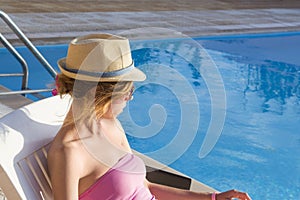 Young girl looking at the swimming pool from the sunbed. Girl at