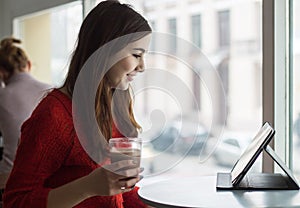 Young girl looking at tablet and smiling in cafe with big windo