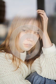 Young girl looking to window feeling sorrowful and unhappy