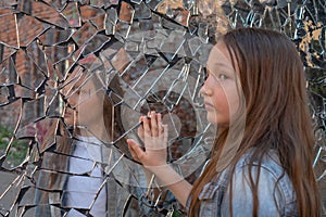 Young girl looks in a broken mirror and shows her hand on a mirror. problems of adolescents. Transitional age