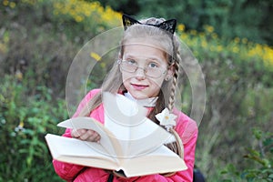 The young girl looks like a teacher - with glasses and a book in her hands. She offers kids more reading books. The concept of