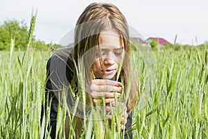 A young girl looks at a spikelet in a sown field