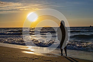 A young girl looks at the sunset by the sea.