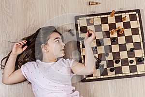 A young girl is lying on the floor next to a chessboard with pieces.