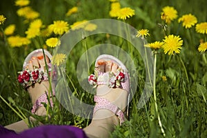 Young girl lying on grass in the middle of dandelions in sunlight with painted toe nails