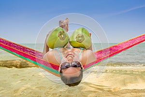 Young girl lying in a hammock holding two coconuts