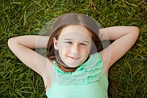 A young girl is lying on her back on the grass looking up.