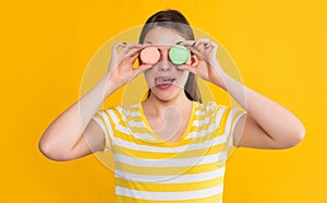 young girl with macaron licking lips on yellow background
