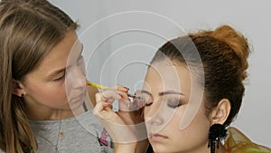 Young girl make-up artist doing professional evening bright makeup to her friend using special brushes