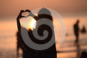 Young girl making love symbol in the sky during sunset