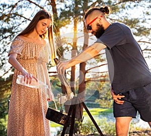 A young girl and a man with a beard in black glasses pour water into a tourist pot for cooking on a campfire. Tourism, outdoor