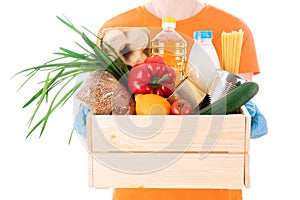 Young girl in a mask and an orange t-shirt holds a wooden box with groceries for delivery isolated on white background