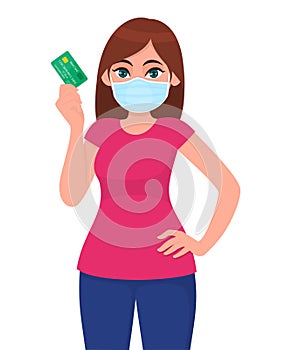 Young girl in medical face mask showing credit, debit card. Woman holding ATM transaction card. Female character. Business