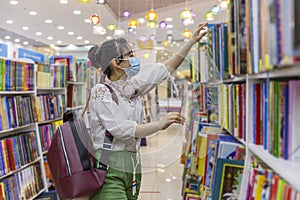 A young girl in a medical mask chooses a book in a bookstore. Knowledge and education. Precautions during the coronavirus pandemic