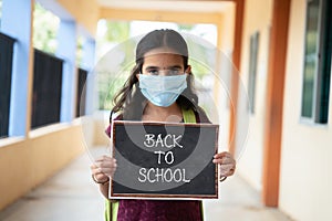 Young girl in medical mask holding back to school signage board at corridor - concept of school reopen, lifestyle and