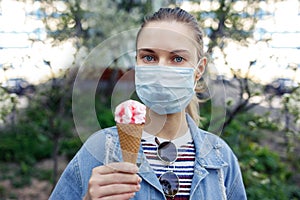 Young girl in medical mask with ice cream in her hands on walk on street