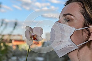 Young girl in medical protective mask sniffs an orchid flower