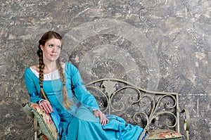 Young girl in medieval dress sits on a banquette