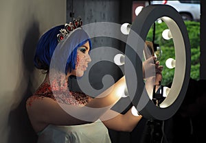 Young girl model in the art make-up like princess in a crown from fairytail makes a selfie in a circle of light photo