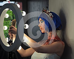 Young girl model in the art make-up like princess in a crown from fairytail makes a selfie photo