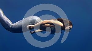 Young girl model underwater mermaid costume on blue background poses in Red Sea.