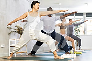 Young girl with multinational group of active people doing stretching exercises during yoga class