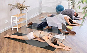 Young girl with multinational group of active people doing stretching exercises during yoga class