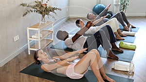 Young girl with multinational group of active people doing stretching exercises during yoga class