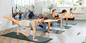 Young girl with multinational group of active people doing stretching exercises during yoga class