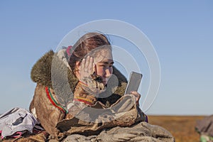 A young girl, in the national winter clothes of the northern inhabitants of the tundra, takes a selfie on a smartphone