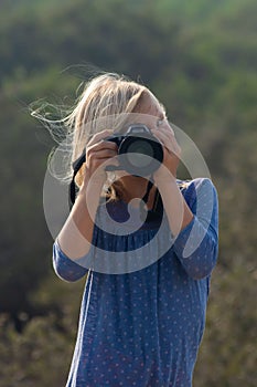 Young girl in nature taking pictures with a large dslr and a zoon lens