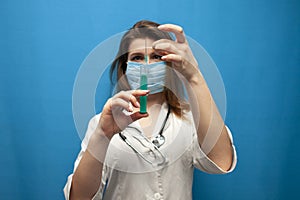 Young girl a nurse in a mask holds a syringe on a blue background, the doctor gives a vaccine, a cure for the disease, virus