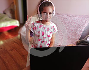 A young girl obey online lessons from her home with the help of headphones and laptop