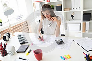 A young girl in the office is holding a pink marker, glasses and working with the documentation.