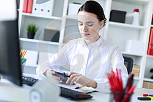 A young girl in the office holds a pen in her hand and works with a calculator, documents and a computer.