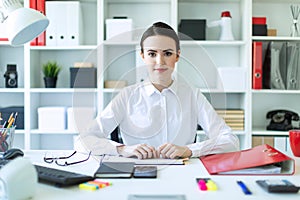 A young girl in the office sits at a table and holds a pen in her hands.