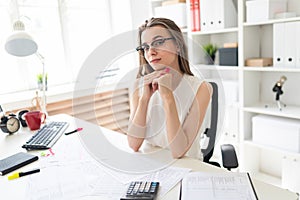 Young girl in the office sits at the table. On the table are documents.