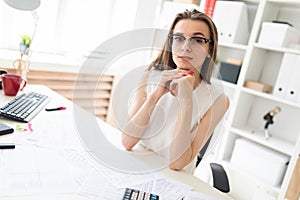 Young girl in the office sits at the table. On the table are documents.