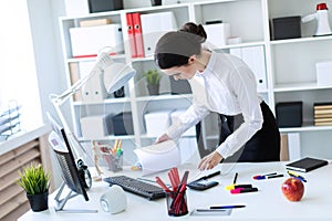 A young girl in the office is standing near the table and looks through the documents.