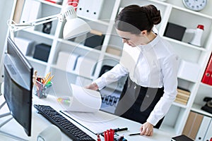 A young girl in the office is standing near the table and looks through the documents.