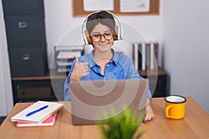 Young girl at the office wearing glasses smiling happy and positive, thumb up doing excellent and approval sign