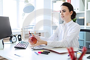 A young girl at the office is working with documents and stretches forth an apple.