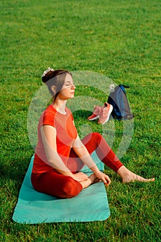 A young girl in orange sportswear for yoga or stretching sitting on a yoga mat in a resting relaxing position with closed eyes.