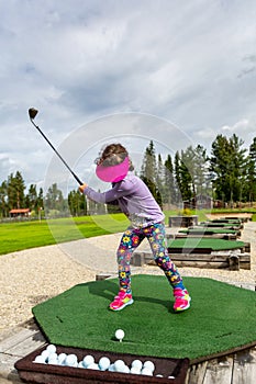 Young girl outdoors at a driving range playing golf and practice her swing.