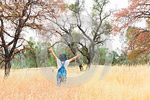 Girl With Overalls and Black Hat Standing in Field With Arms Raised