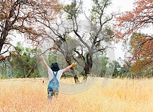 Girl With Overalls and Black Hat Standing in Field With Arms Raised